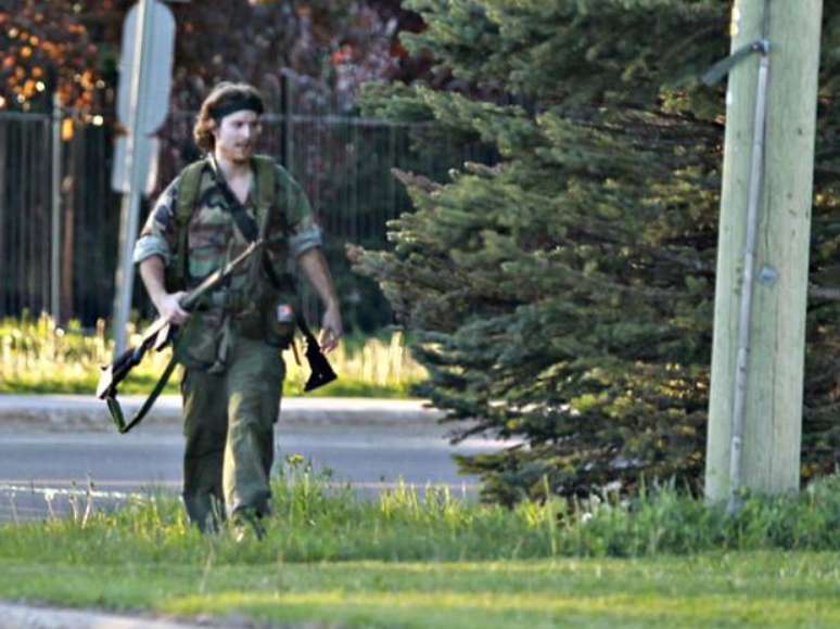 <p>Uma fotografia divulgada pela imprensa local mostra o suspeito, vestido com roupas militares camufladas e portando ao menos duas armas automáticas</p>