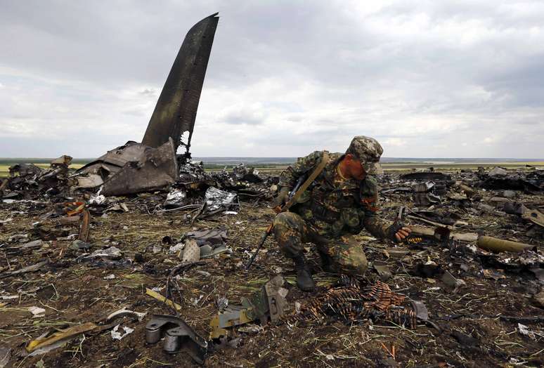 <p>Um separatista pró-russo reúne munições no local onde um avião de transporte do Exército ucraniano, modelo Il-76, foi derrubado, em Lugansk, neste sábado, 14 de junho</p>