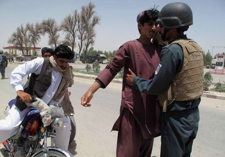 <p>Policial afegão revista passageiros em um posto de controle na província de Helmand, em 25 de junho, quando mais de 800 insurgentes talibãs lançaram uma grande ofensiva no sul do Afeganistão para tentar ganhar território recentemente desocupado pelas tropas dos EUA</p>