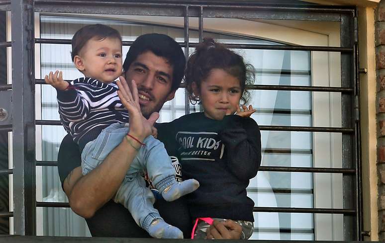 O atacante uruguaio Luis Suárez atende torcedores com os filhos Benjamin e Delfina da janela da casa da mãe em Lagomar, cidade próxima a Montevidéu. O jogador foi recepcionado por centenas de fãs após ser suspenso pela Fifa por nove jogos e por quatro meses de qualquer atividade relacionada ao futebol pela mordida dada no zagueiro italiano Chiellini. O presidente uruguaio José Mujica foi um dos que compareceu ao aeroporto para receber o atacante