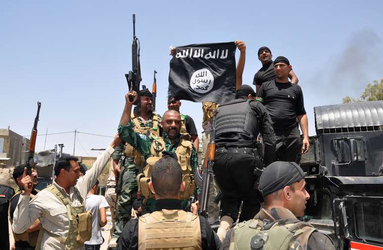 <p>Forças de segurança iraquianas seguram uma bandeira do Estado Islâmico do Iraque e do Levante capturada durante uma operação em Dallah Abbas, ao norte de Baquba, em 28 de junho</p>
