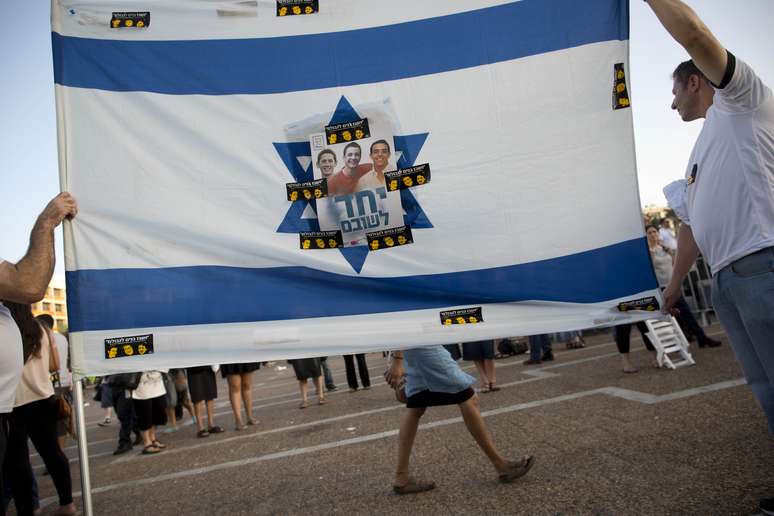 <p>No centro de uma bandeira de Israel, fotos dos três jovens desaparecidos são coladas em memória deles</p>