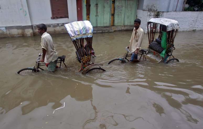 <p>Pessoas caminham em uma rua inundada após pesadas chuvas em Agartala, capital do estado de Tripura, nordeste da Índia, em 11 de junho. A região é afetada por um surto de Malária</p>