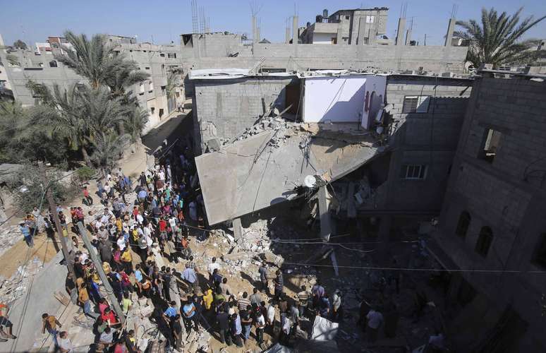 <p>Palestinos se reúnem em torno de uma casa que, segundo a polícia, foi destruída em ataques aéreos israelenses em Khan Younis, no sul da Faixa de Gaza, em 8 de julho</p>
