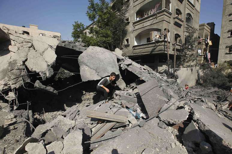 Palestino caminha sobre destroços de casa destruída por bombardeio israelense