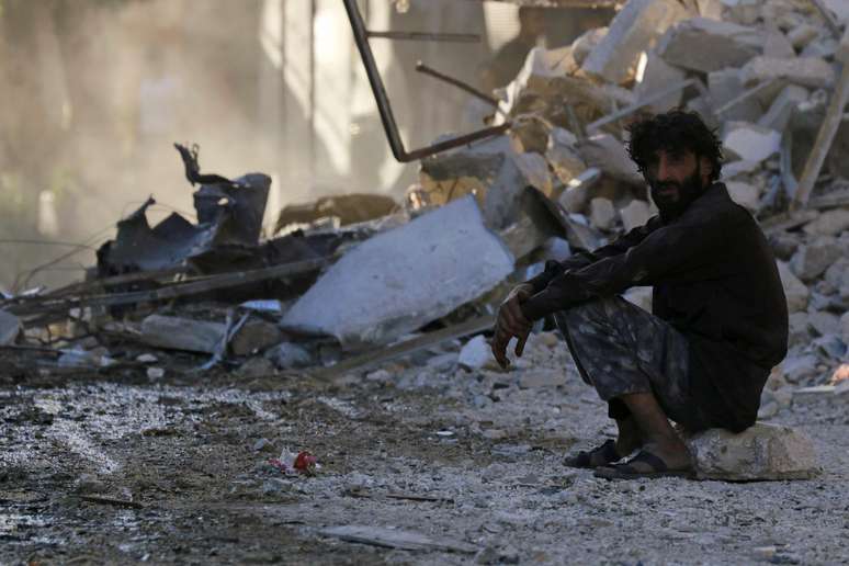 <p>Um homem senta-se em um local destruído pelo que ativistas disseram ser uma bomba lançada por forças leais ao presidente Bashar al-Assad, no bairro al-Myassar, cidade de Aleppo, Síria, em 10 de julho</p>