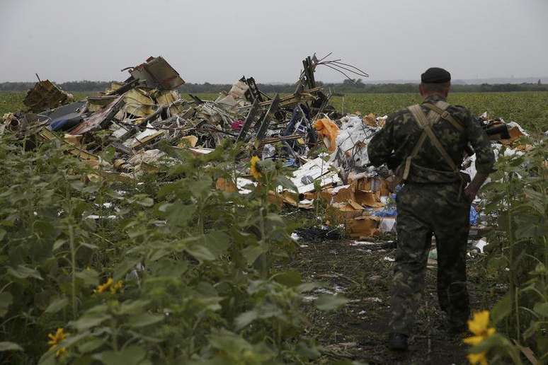 <p>Separatista ucraniano observa um dos v&aacute;rios campos de destro&ccedil;os do voo MH17</p>