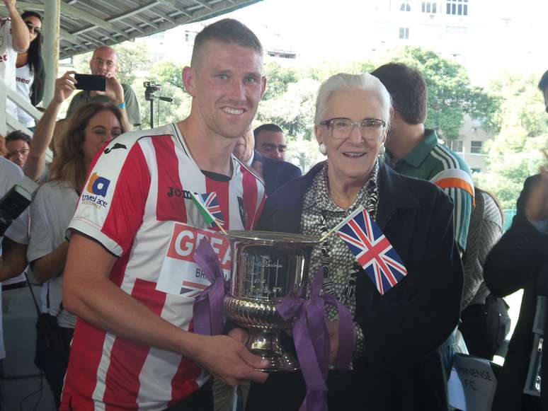 <p>Capitão do Exeter, Scott Bennett, exibe a taça com a "fita roxa" - apelido do goleiro do Brasil há 100 anos, Marcos Mendonça</p>