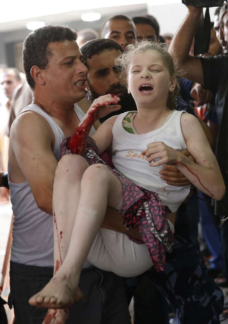 <p>Um palestino carrega uma menina ferida na sala de emergência do Hospital Shifa, no norte da Faixa de Gaza, em 20 de julho</p>