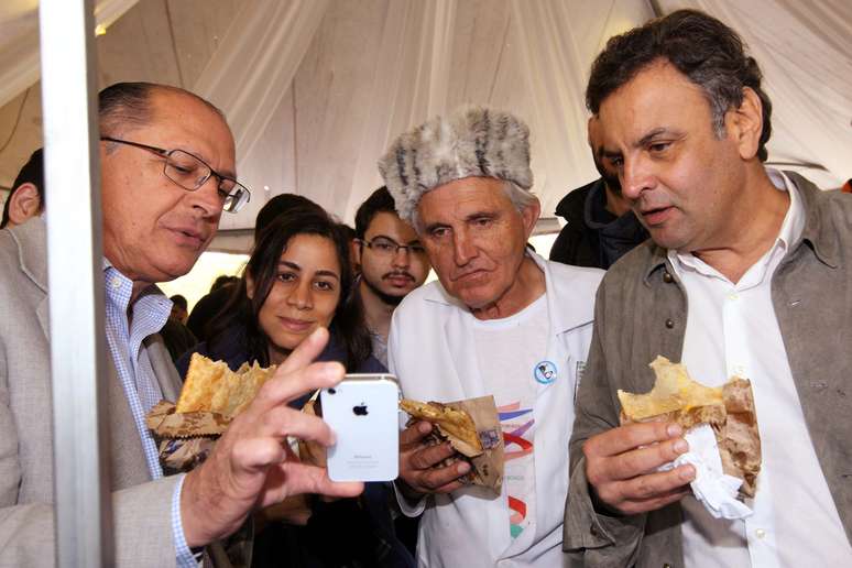 <p>Geraldo Alckmin (esq), o padre Rosalvino Morán (centro) e Aécio Neves comem pastel na Feira Tecnológica</p>