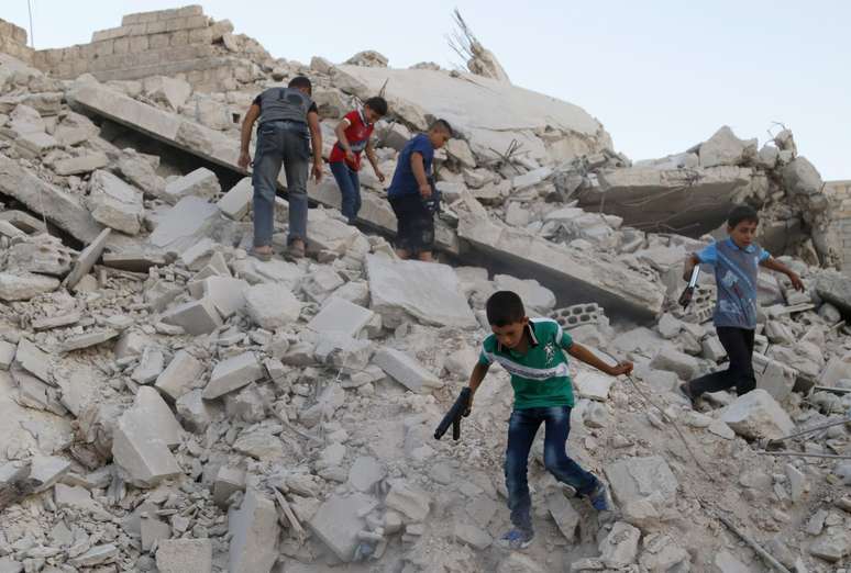 <p>Meninos seguram armas de brinquedo e brincam sobre os escombros de edifícios destruídos em Maarat Al-Nouman, ao sul de Idlib, na Síria, em 29 de julho</p>