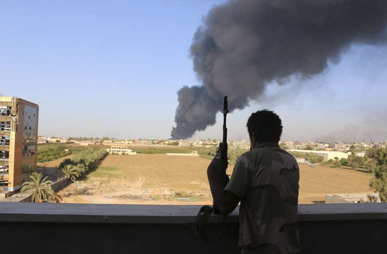 <p>Integrante da milícia Zintan observa um tanque de combustível pegar fogo após o diparo de foguetes em Trípoli, em 2 de agosto</p>