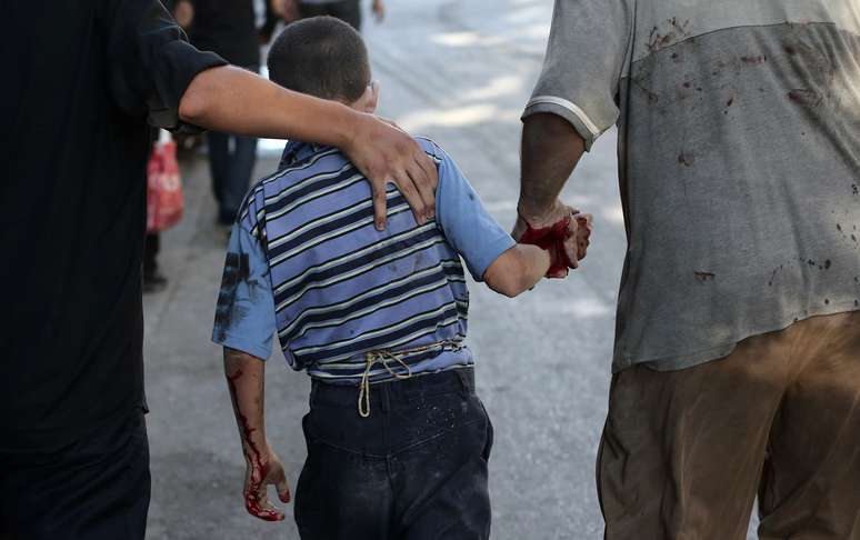 <p>Homens sírios caminham ao lado de um menino ferido após um bombardeio das forças do governo em Duma, em 3 de agosto</p>