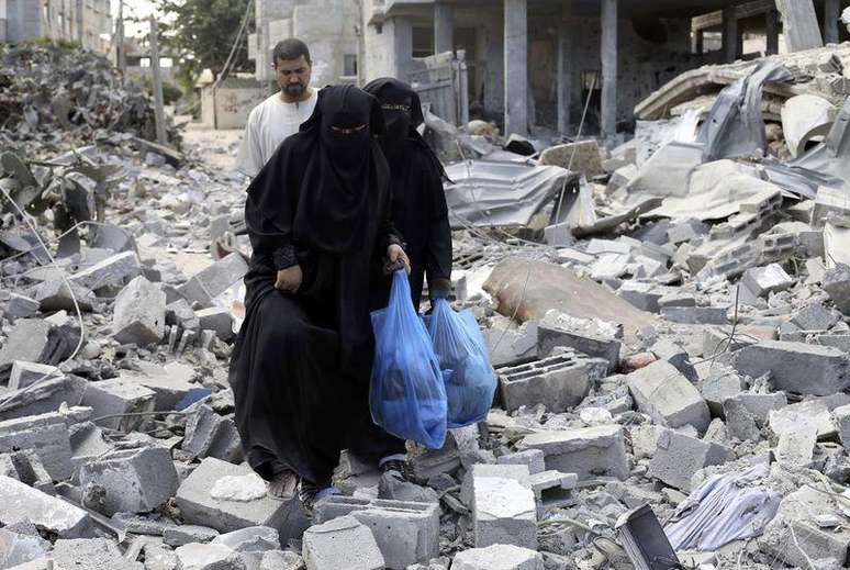 <p>Palestinas caminham sobre destro&ccedil;os de casa em Rafah que, segundo testemunhas, foram destru&iacute;das por ataque de Israel</p>
