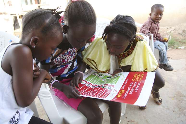 <p>Meninas olham&nbsp;para um cartaz, distribu&iacute;do pela Unicef, tendo informa&ccedil;&otilde;es e ilustra&ccedil;&otilde;es das melhores pr&aacute;ticas que ajudam a prevenir a propaga&ccedil;&atilde;o do Ebola, na cidade de Voinjama, em Lofa County, na Lib&eacute;ria</p>