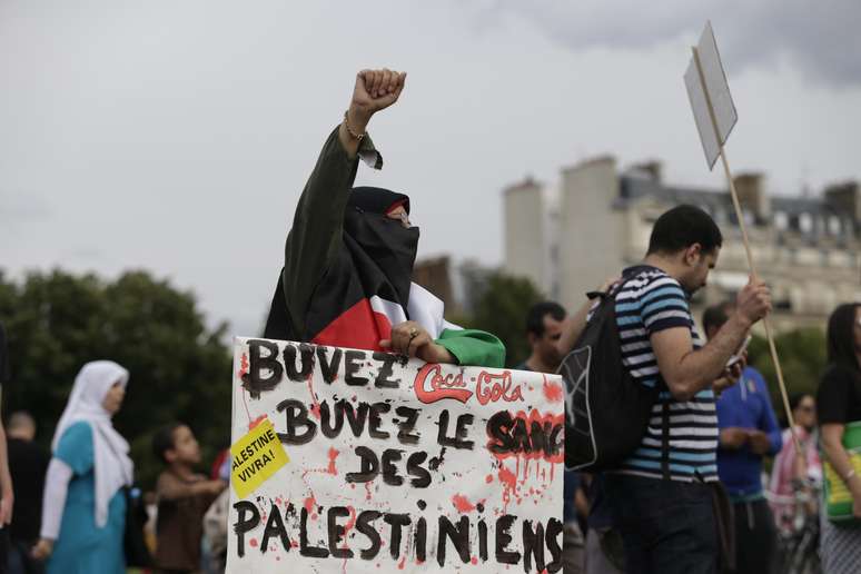 Manifestante ergue o braço enquanto segura um cartaz que diz "Beba Coca-Cola, beba sangue de palestinos", em Paris