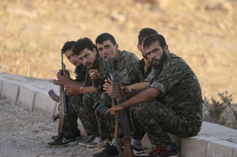 Oficiais curdos sentam em campo militar ao norte do Iraque durante evacuação de refugiados em Sinjai