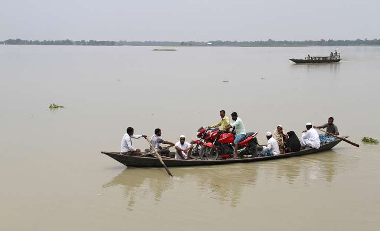Pessoas transportam pertences em pequeno barco em meio às inundações no norte da Índia