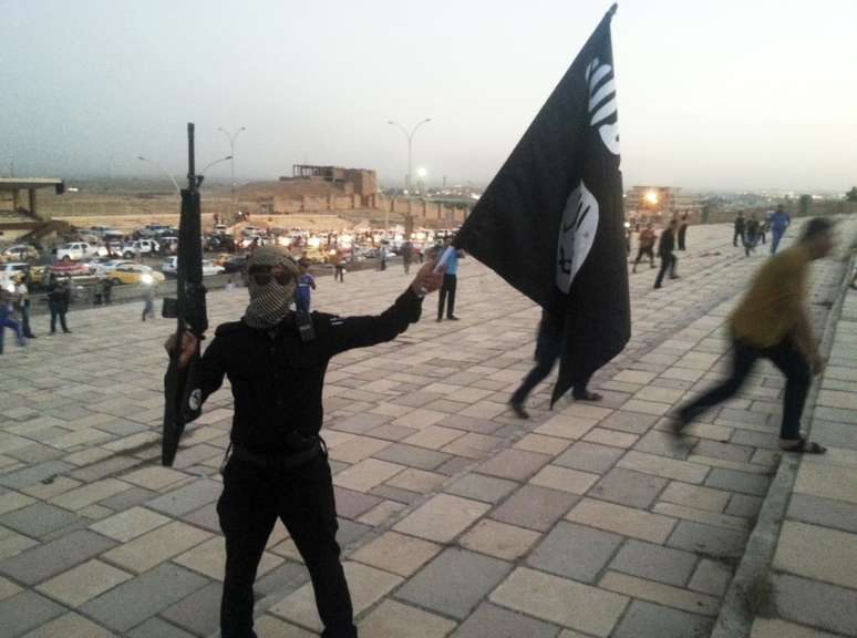 <p>Um integrante do Estado Isl&acirc;mico exibe&nbsp;uma bandeira do grupo terrorista em uma rua da cidade de Mossul, em 23 de junho</p>
