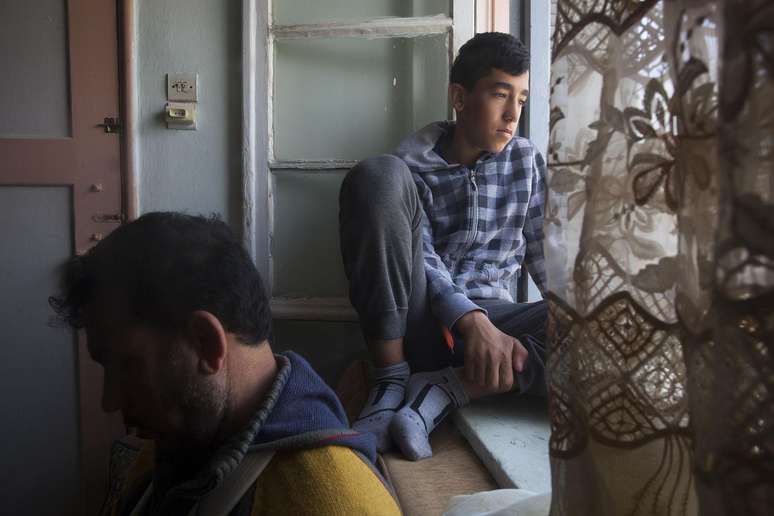 Malak, 13, olha pela janela do apartamento onde mora com seu pai e outros dois refugiados em Atenas