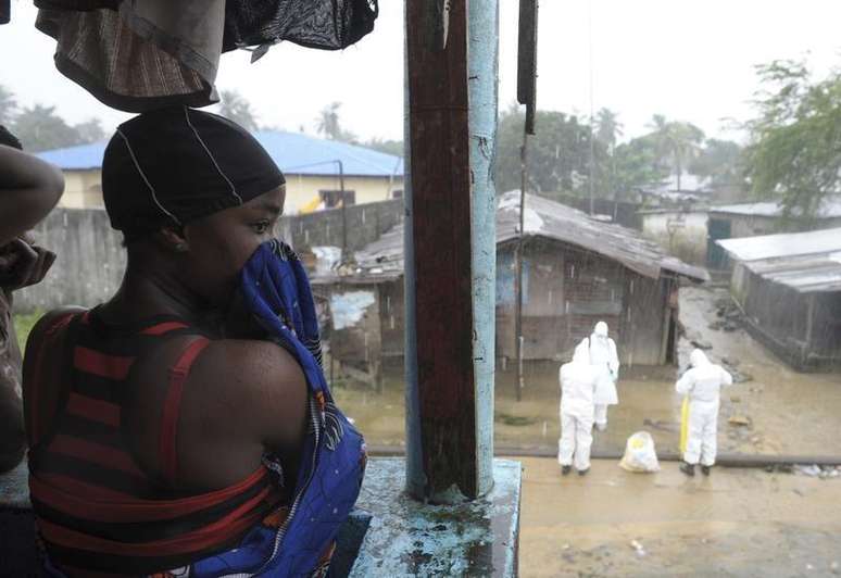 Mulher observa trabalhadores de saúde com roupas especiais em mercado de Monróvia. 17/08/2014