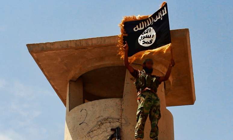 <p>Militante do Estado Isl&acirc;mico exibe bandeira do grupo jihadista em local rec&eacute;m-conquistado no Iraque</p>