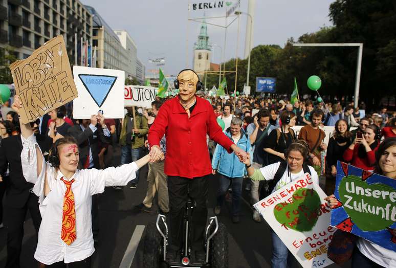 <p>Um manifestante usa uma máscara da chanceler alemã, Angela Merkel, dutante a passeata realizada em Berlim</p>