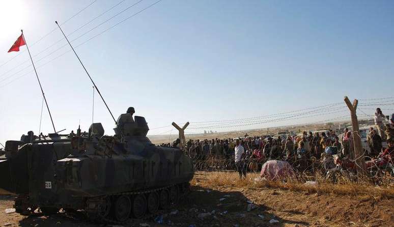 Curdos sírios aguardam na fronteira diante de soldados turcos nesta segunda-feira. Milhares deles têm fugido devido ao avanço do Estado Islâmico.