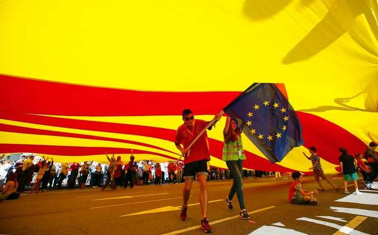 <p>Manifestantes carregam&nbsp;bandeira da Uni&atilde;o Europeia sob uma bandeira gigante da Catalunha durante protesto em Barcelona, no Dia Nacional da Espanha</p>