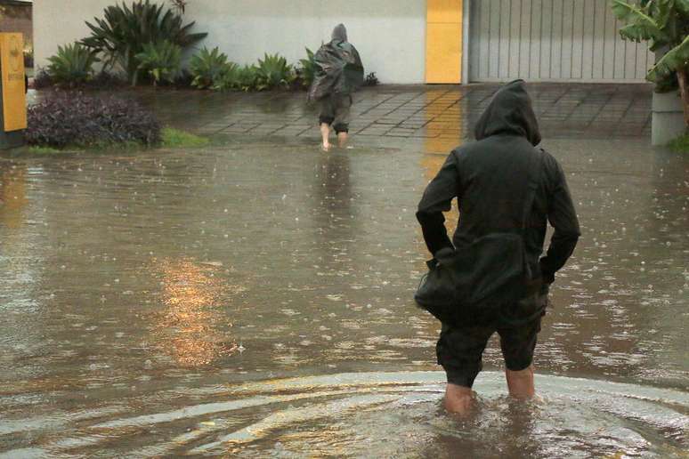 Homem tenta atravessar a rua alagada em Porto Alegre em dia de temporal