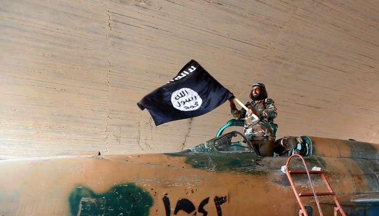 <p>Combatente do Estado Islâmico ergue uma bandeira da organização terrorista em cima de um caça, em agosto deste ano</p><p> </p>