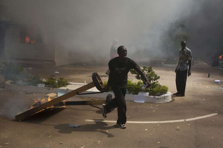 <p>Um manifestante carrega um objeto em chamas fora do edifício do Parlamento em Ouagadougou, capital de Burkina Faso, em 30 de outubro </p>