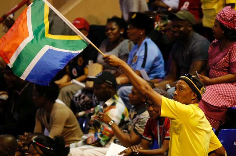 <p>Homem ergue bandeira da &Aacute;frica do Sul em cerim&ocirc;nia de homenagem a Senzo Meyiwa e outros esportistas sul-africanos mortos recentemente</p>