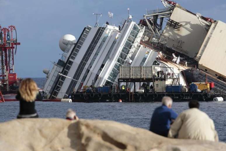 <p>Pessoas olham navio de cruzeiro Costa Concordia tombado na costa da Toscana, na It&aacute;lia</p>