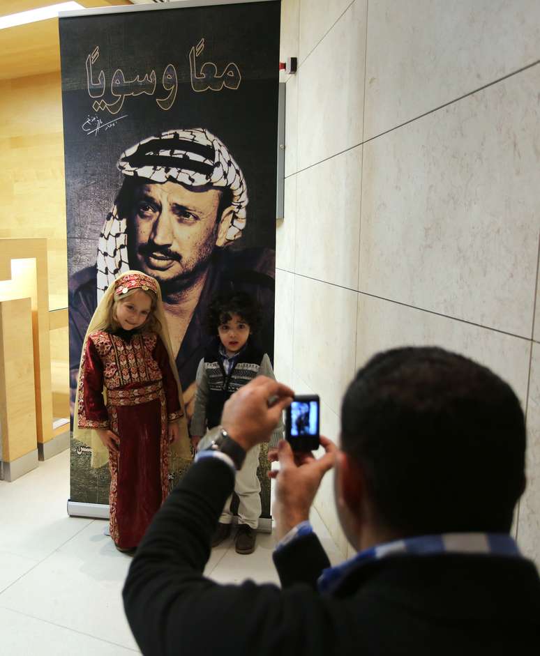 <p>Crian&ccedil;as posam para&nbsp;foto em frente a um cartaz com a imagem do falecido l&iacute;der palestino Yasser Arafat, durante a abertura de um museu de Arafat na cidade de Ramallah, na Cisjord&acirc;nia</p>