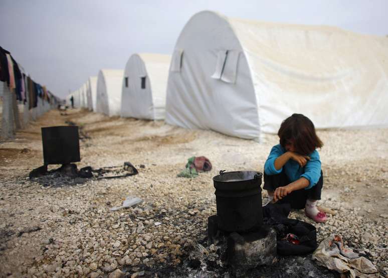 Criança curda, na Turquia, senta próximo de barracas dos sírios refugiados