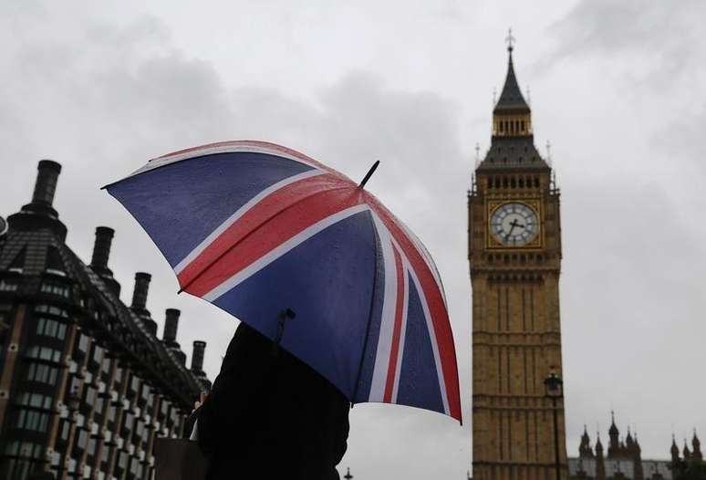 <p>Uma mulher com guarda-chuva nas cores da bandeira do Reino Unido à frente do Big Ben</p>