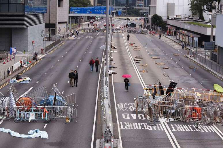 <p>Pedestres passam por obst&aacute;culos e barricadas colocadas por manifestantes em avenida de Hong Kong</p>