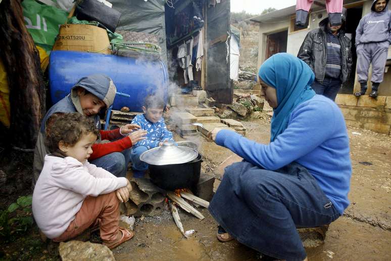 <p>Mulher prepara comida junto dos filhos próximo à tenda onde vive no campo destinado a refugiados que deixaram a Síria por causa da guerra civil, na cidade montanhosa de Ketermaya, no Líbano</p>