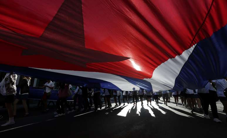 Estudantes cubanos carregam uma bandeira gigante de seu país durante passeata em Havana.