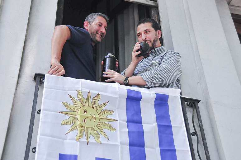 Um ex-prisioneiro de Guantánamo (direita), toma mate na varanda de uma casa, junto a bandeira do Uruguai, em Montevidéu