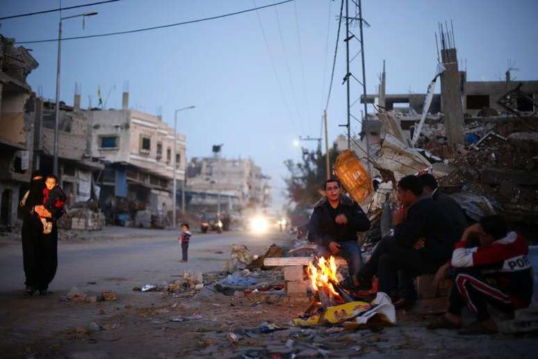 Palestinos se esquentam em uma fogueira perto dos escombros de casas que dizem terem sido destruídas em bombardeios de Israel, durante o mais recente conflito entre israelenses e mlitantes do Hamas, em Gaza. 1/12/2014.