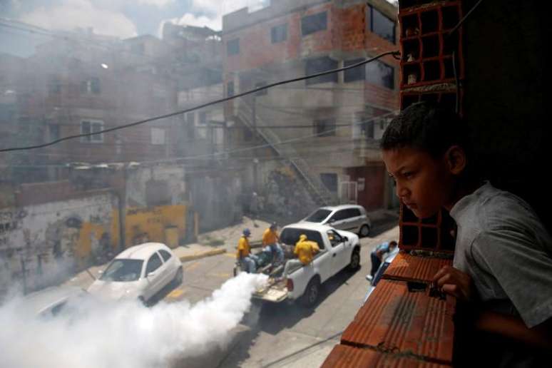 Menino observa trabalhadores aplicando remédio contra mosquito da dengue em rua de Caracas. 22/09/2014