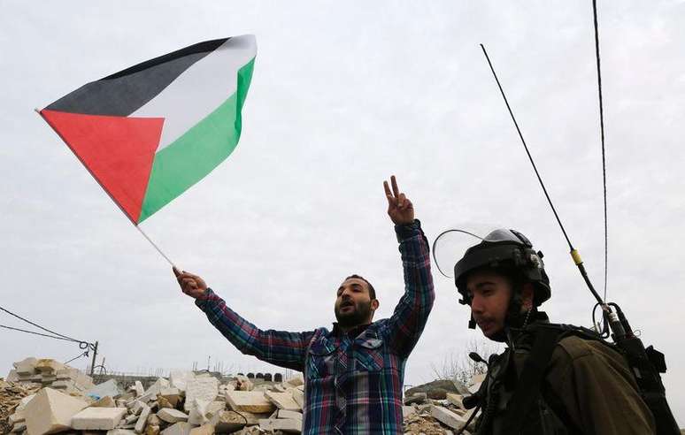 Manifestante palestino segura uma bandeira da Palestina perto de um soldado israelense. 19/12/2014
