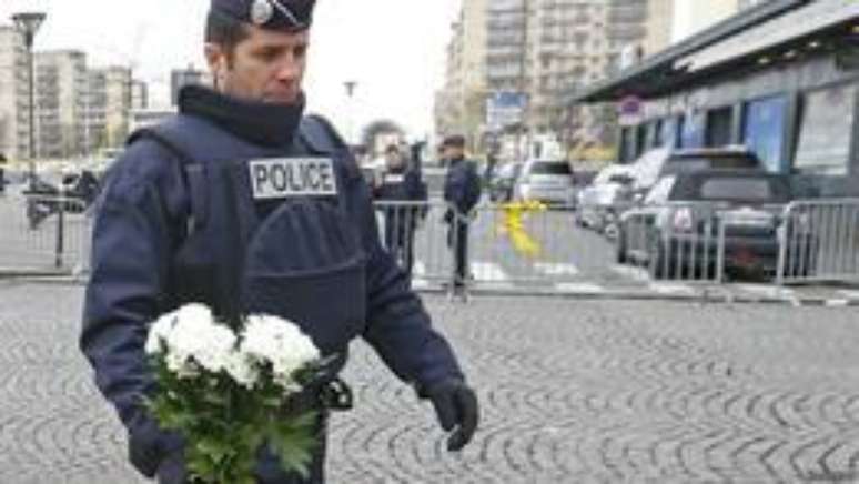 Policial deposita flores em supermercado atacado por extremista (foto: Reuters)