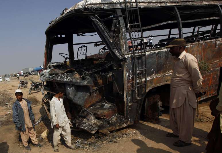 Curiosos olham os destroços do ônibus que colidiu com uma caminhão que transportava gasolina, matando 57 pessoas, no Paquistão
