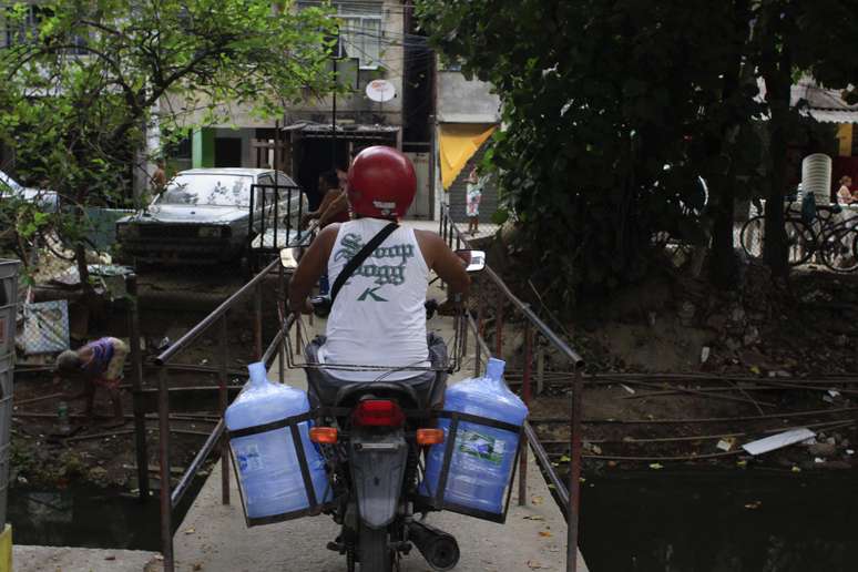 Moradores abastecem galões com água potável de uma bica no canal