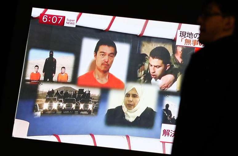 Homem passa por tela de TV exibindo imagens do piloto jordaniano Kasaesbeh e do jornalista japonês Goto, em Tóquio. 29/01/2015