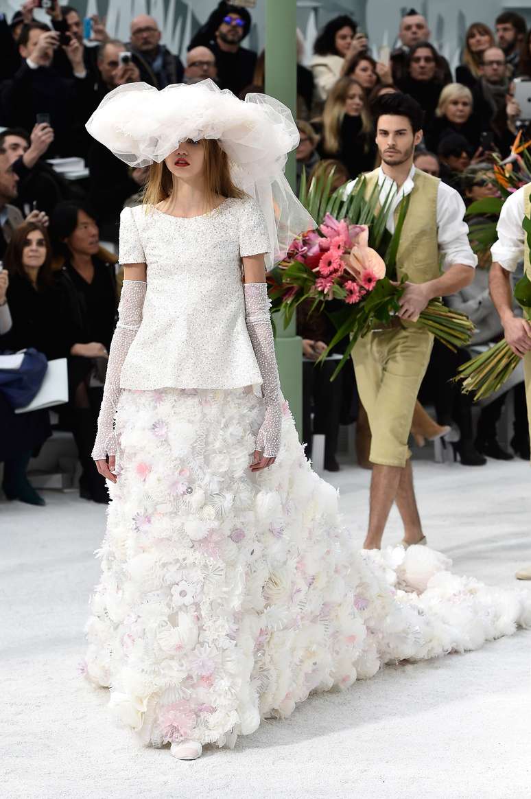 O vestido de noiva proposto por Karl Lagerfeld para Chanel trás saia com cauda, blusa com cristais, luvas e chapéu de tule no lugar do véu