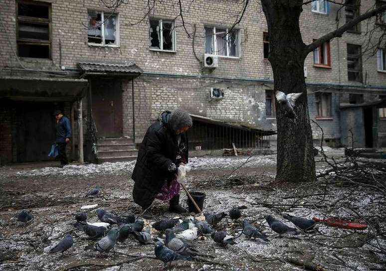 Mulher alimenta pombos diante de casa destruída em Debaltseve, leste da Ucrânia. 05/02/2015.